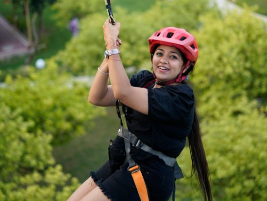 Woman on a zipline ride at inflated trampoline surrounded by trees at Themis Mudhouse - A Nature's Retreat Resort & Wellness