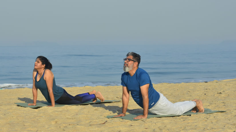 a couple performing Yoga on the beach with the sea in the background - Heritage Village Resort & Spa, Goa