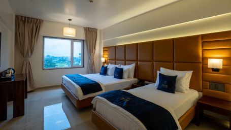 Side view of two beds in Family Premium with bedside tables scenic view from windows with curtains - Mastiff Grand - The Sia Palace Suites Banquets Khopoli