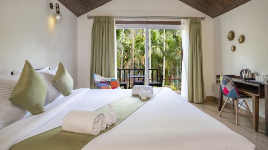 A hotel room featuring a king size bed, a workstation with a chair, and a view overlooking the pool - Stone Wood Nature Resort, Gokarna