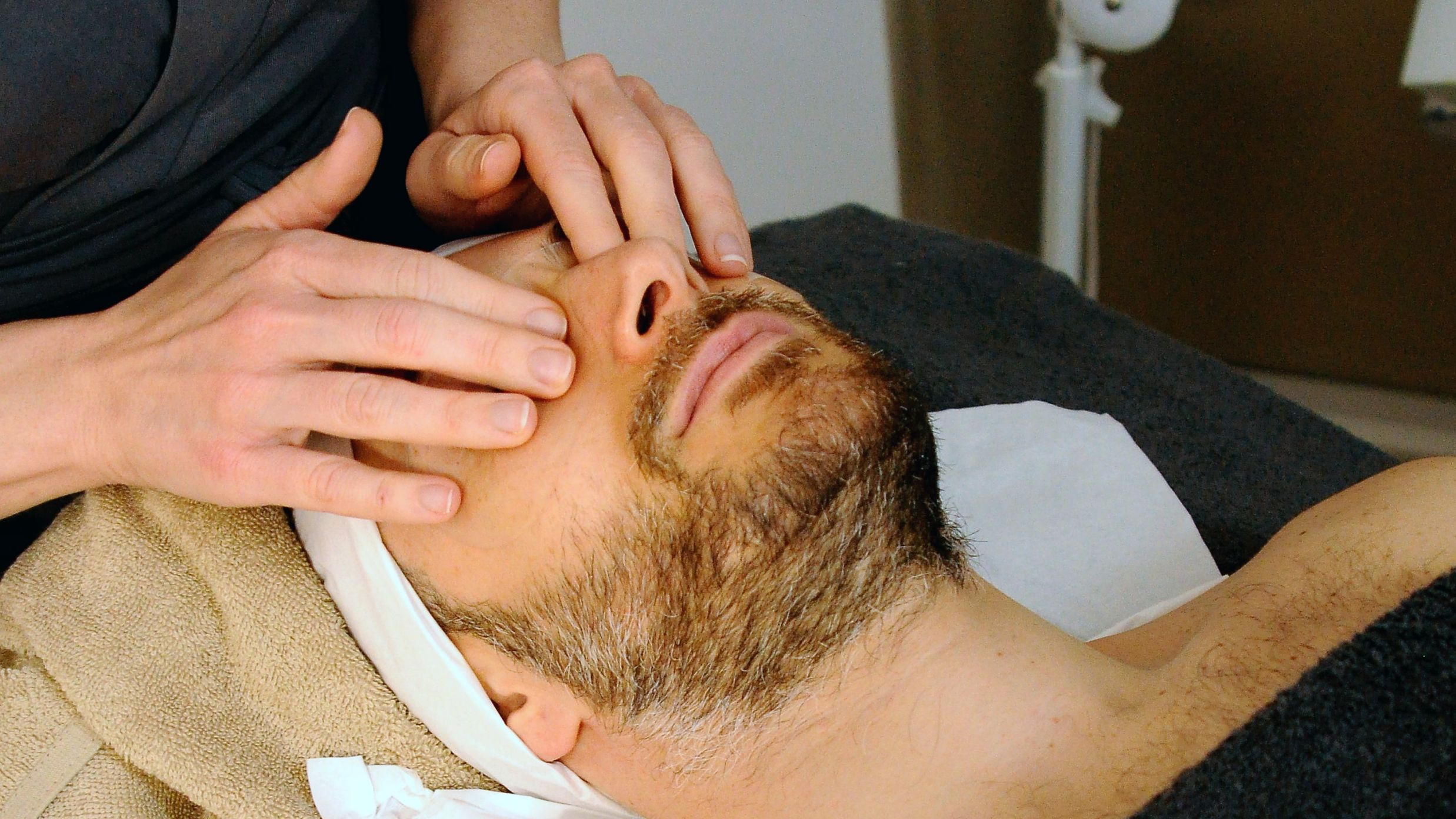 A man receiving facial massage from a masseur