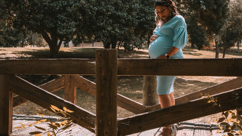 A pregnant mother looking at her baby bump standing on a wooden bridge