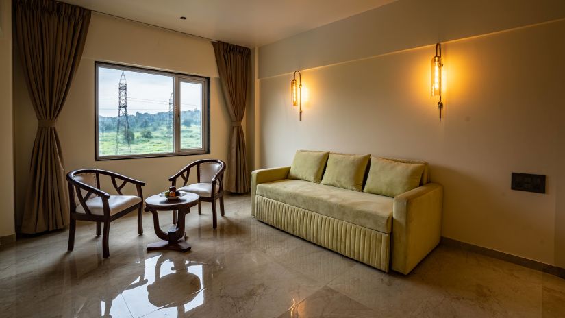 View of Suite living room with sofa set coffee table and large window looking over scenic view - Mastiff Grand - The Sia Palace Suites Banquets Khopoli