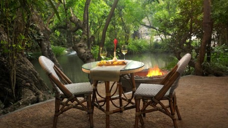 An outdoor dining setup by a tranquil river-Amanvana Spa Resort, Coorg - Luxury Resort