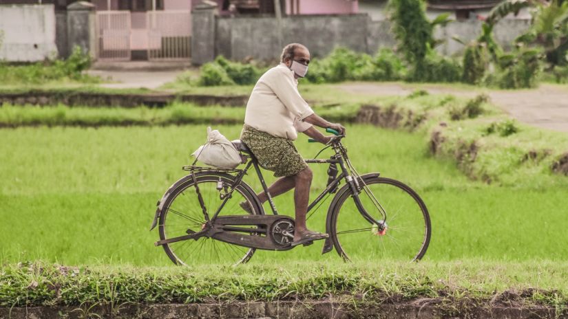 A traditional villager in Kerala riding a bicycle with houses in the background