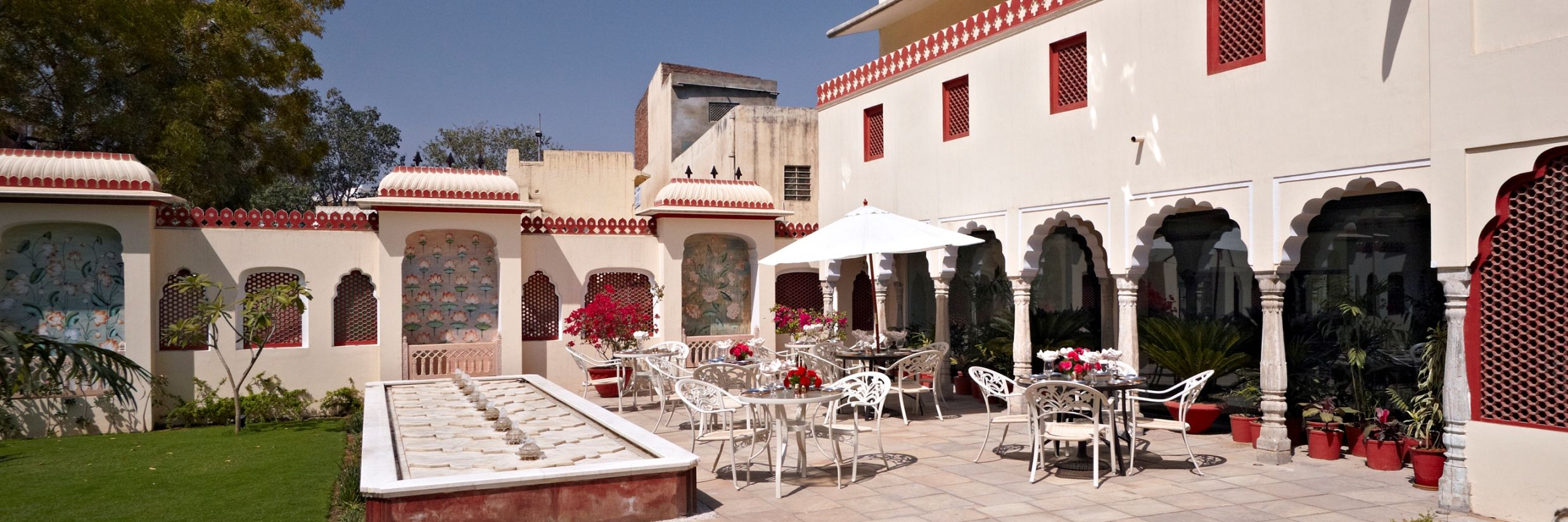 Seating arrangments in an open air setting with a fountain next to grass - Mandawa Haveli, Jaipur