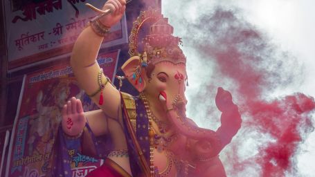 a ganesha's idol kept on a chariot while going for a visarjan with colours being thrown on it