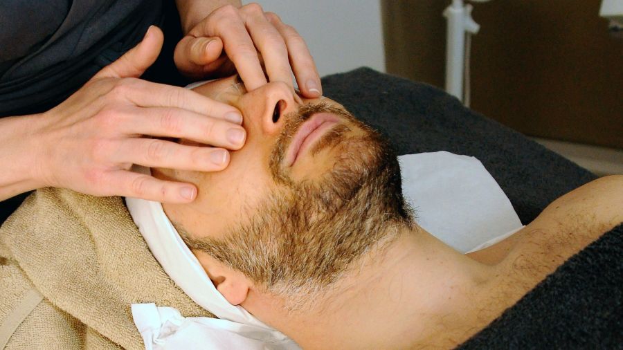 A man receiving facial massage from a masseur