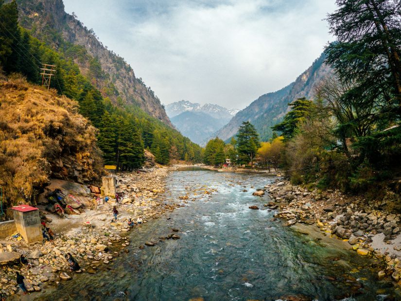 a shallow river with rocks on the bottom and clear water and mountains in the vicinity