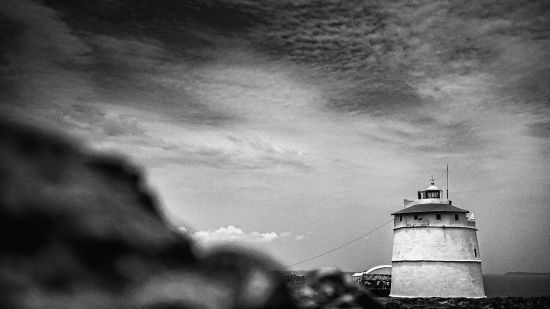 a greyscale image of a lighthouse with dark clouds above it