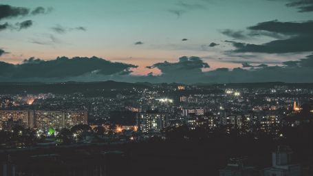 An expansive perspective of a city skyline in the evening, accompanied by sporadic clouds and a twilight sky. -Fort JadhavGADH 