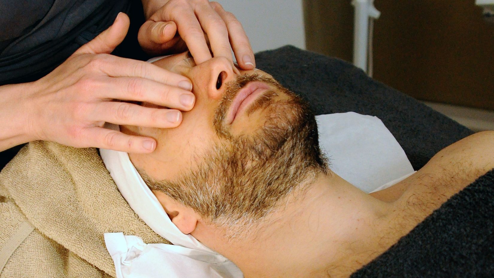 A man receiving facial massage from a masseur