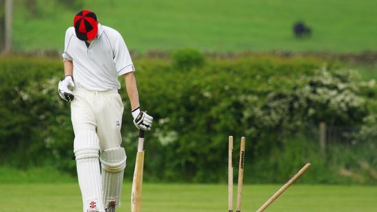 a man wearing a white coloured jersey holding a cricket bat standing next to the wicket