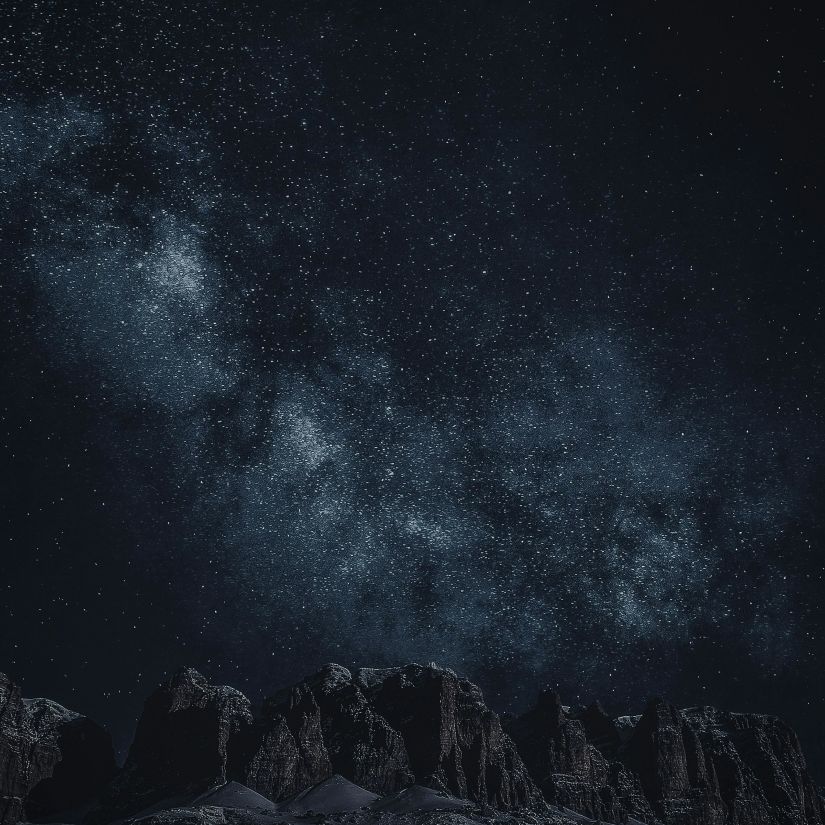 The Milky Way stretches across the night sky above silhouetted mountains.