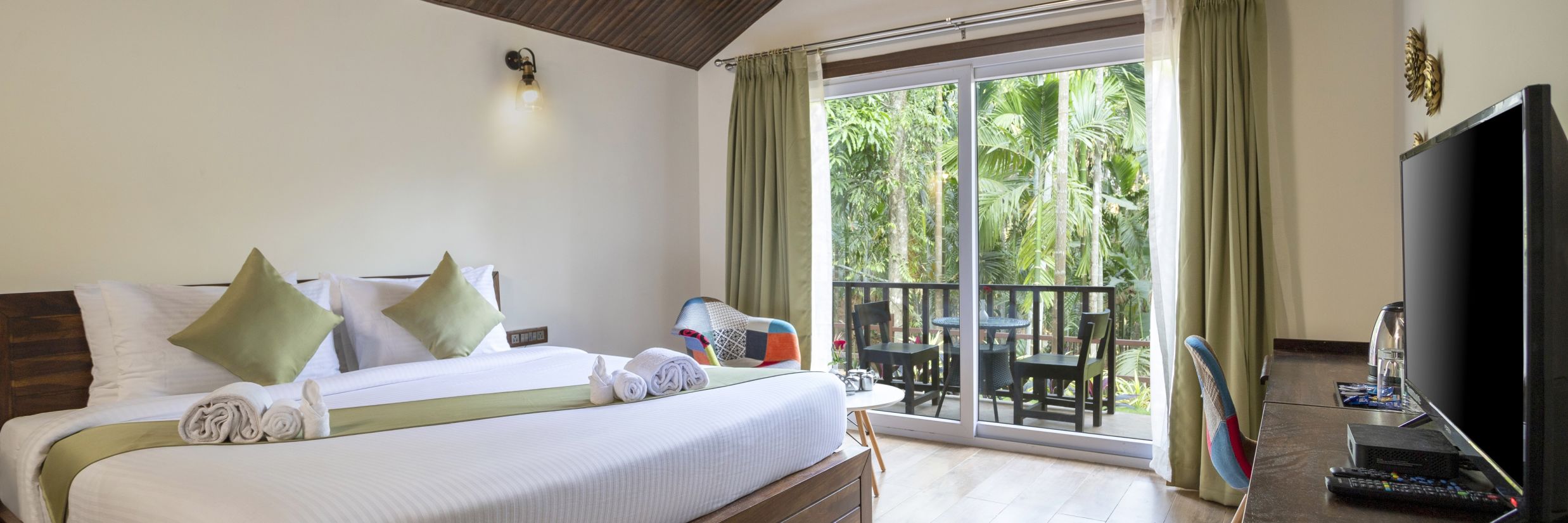 A hotel room with a garden view, a wall mounted television and a large bed - Stone Wood Nature Resort, Gokarna