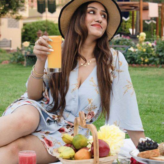 Heritage Village Manesar - A female model holding a glass of orange coloured beverage and with lush greenery in the background