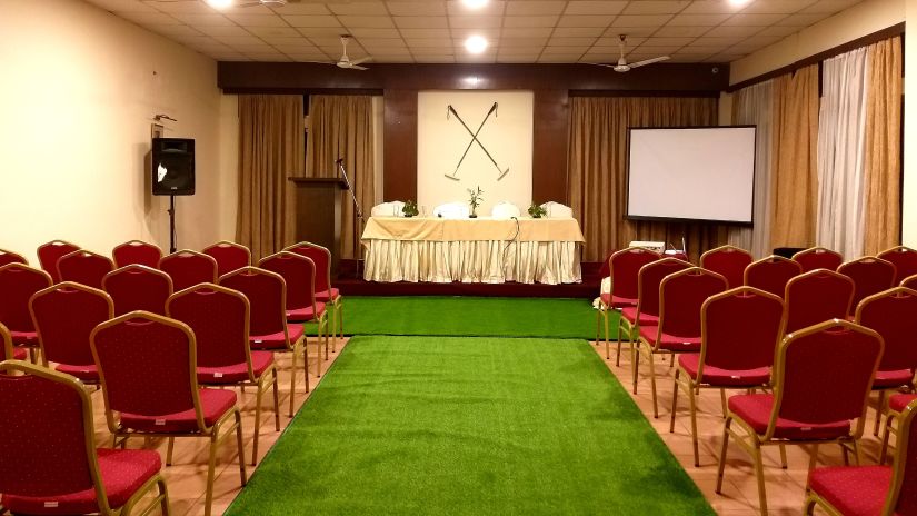 A conference room with rows of red chairs, a podium, and a projection screen.