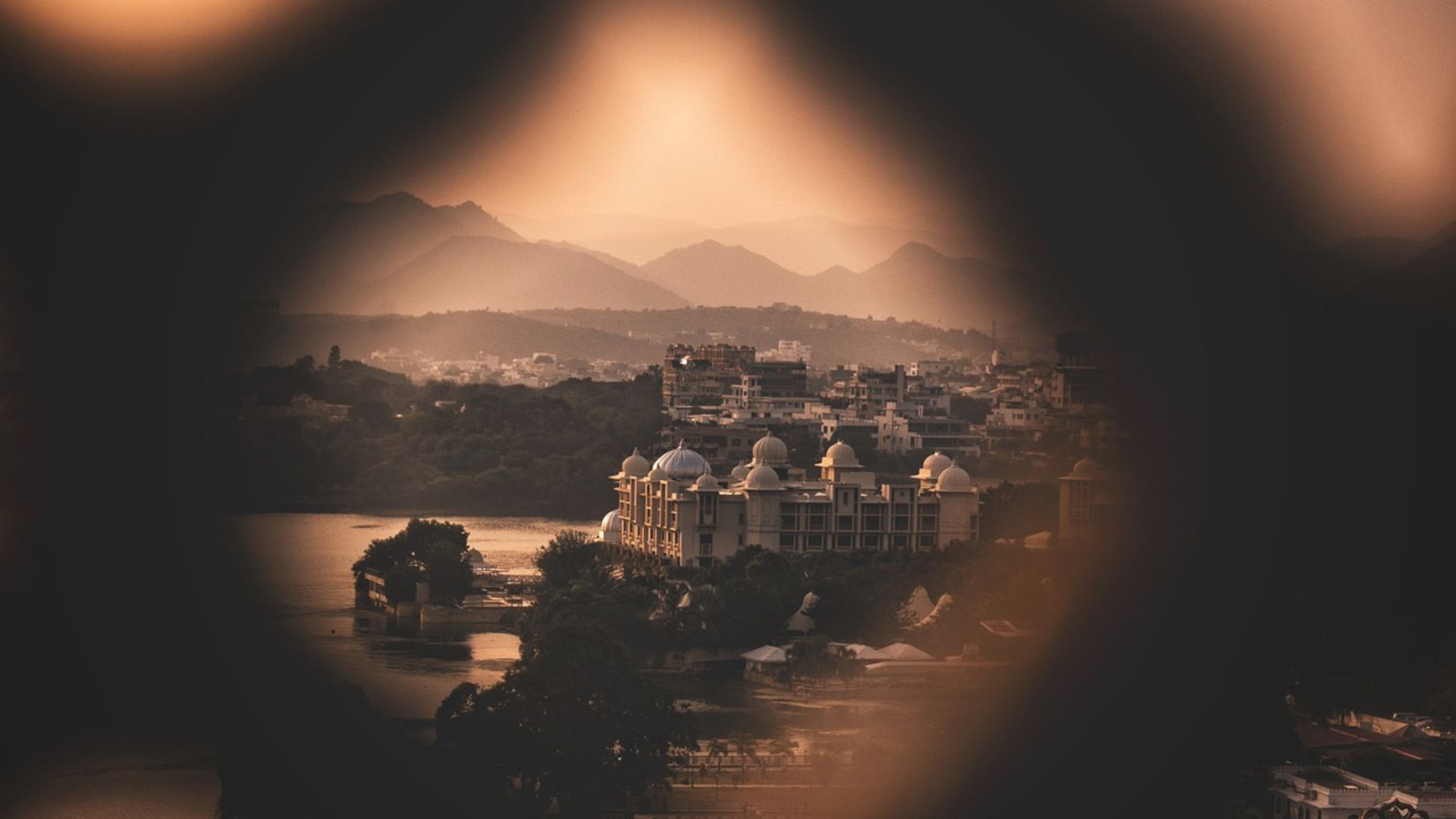 A blurry foreground revealed the Udaipur metropolis, with the shadows of mountains and the brightness of lights in the backdrop - Udaipur