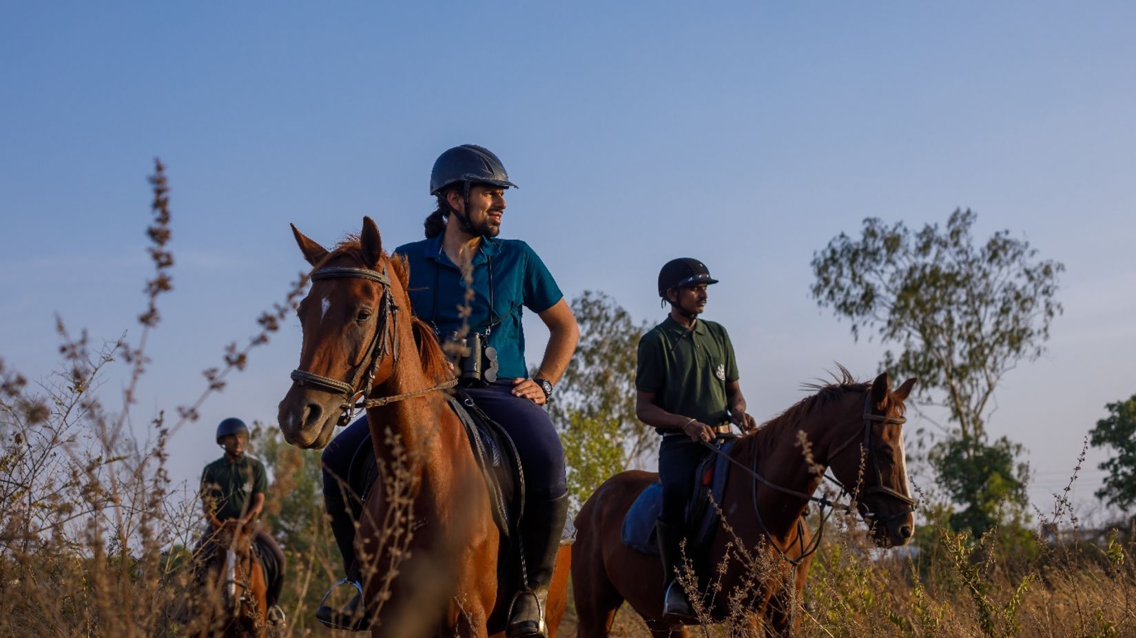 3 people riding horses in a field