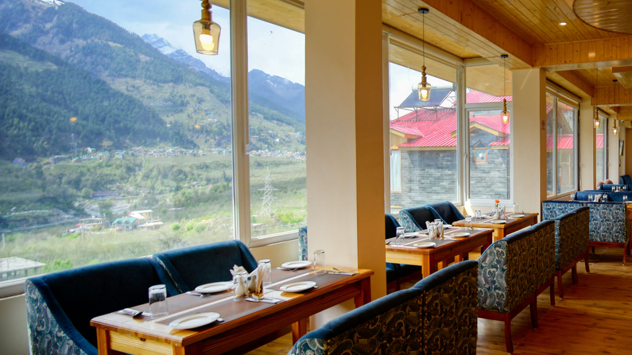 Dining arrangement besides windows with mountain views - Clarks Inn Suites, Manali