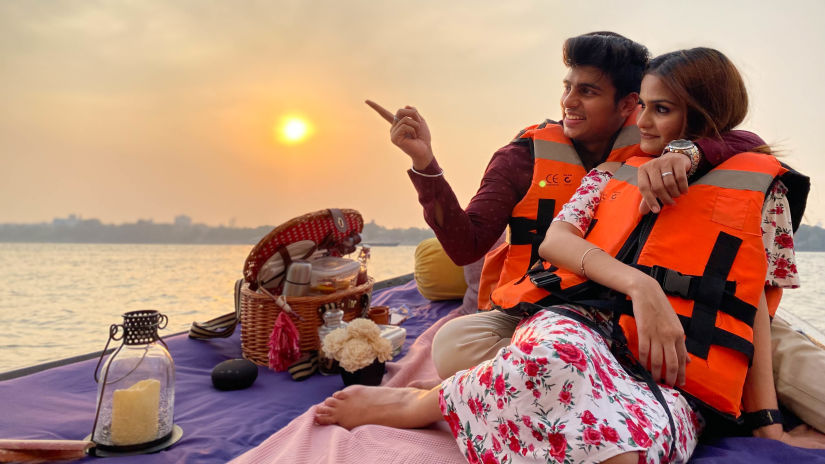 a couplle having a picnic on a boat wearing life vests and the sun setting in the background - Polo Floated Kolkata