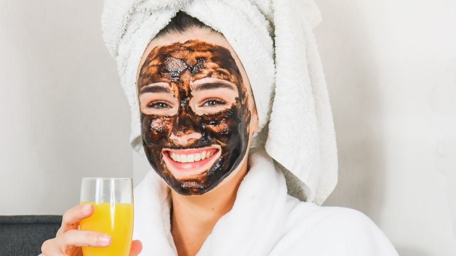 a woman with a face mask in bathrobe holding a glass of juice 