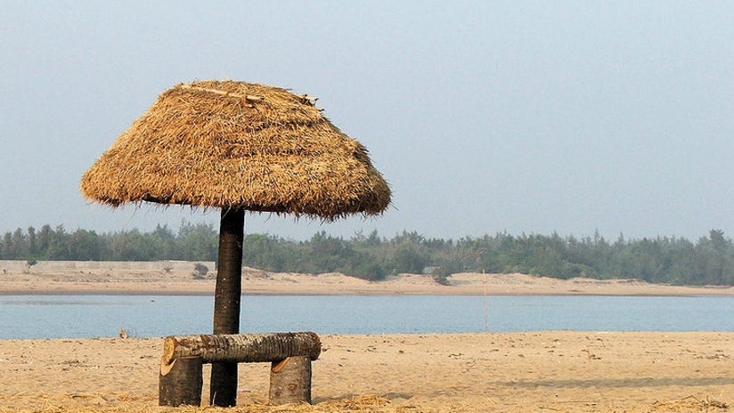 A view of water body and small sitting place made of stone and umbrella  made of dry leave beach resort at Lotus Eco resort Konark 