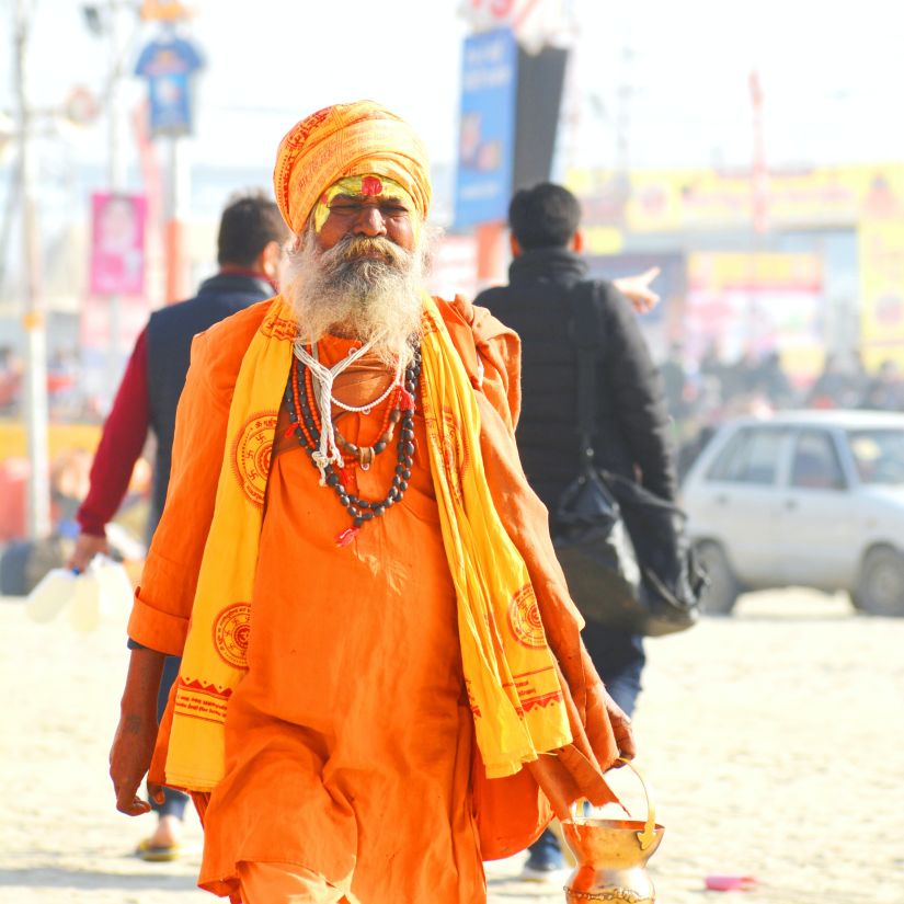 A saint walking down the road dressed in orange clothes and holding his bag -  Prayagraj.