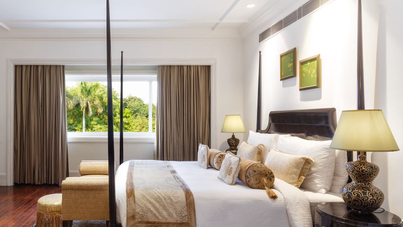 side view of a bedroom with large windows and a large bed with side drawers - The Claridges, New Delhi 