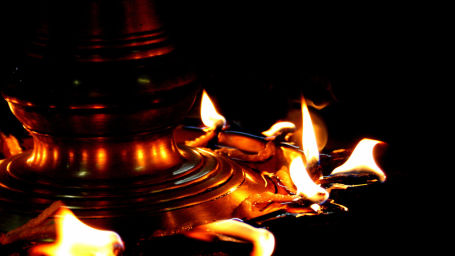 Flames dancing from a traditional brass oil lamp, casting a warm glow that symbolises light and spirituality in the darkness.