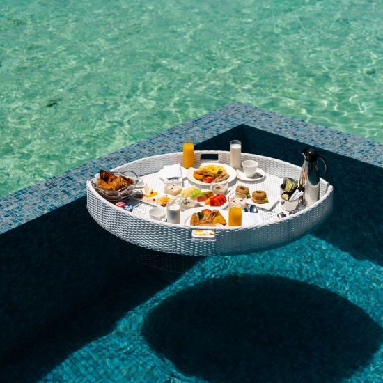 a floating breakfast tray floating on an infinity swimming pool with the ocean in the background