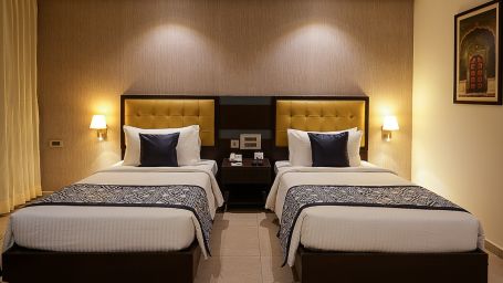 Two plush twin beds in our royal suite room illuminated by bright yellow lights - Grand Continent, Malleshwaram