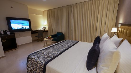 A view of our deluxe room with a large bed, a sofa and a wall mounted television - Grand Continent, Malleshwaram