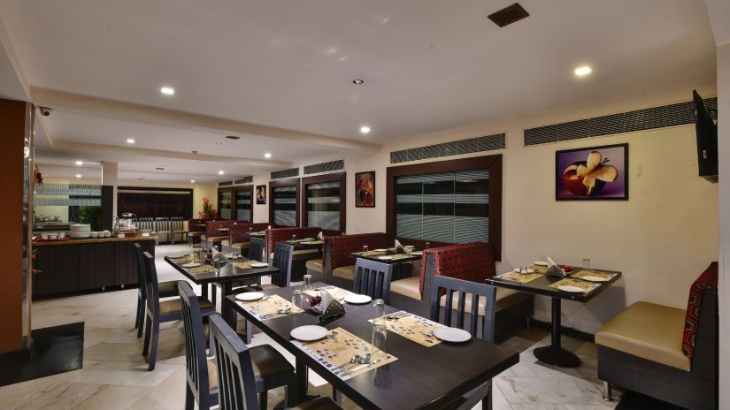 A well-lit dining area with tables set for service - Click hotels Yuvraj, Surat