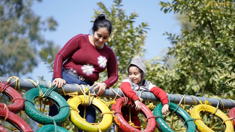 A woman helping a kid with tyre course at inflated trampoline surrounded by trees at Themis Mudhouse - A Nature's Retreat Resort & Wellness