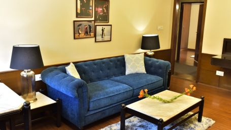 A living room featuring a blue sofa, a coffee table and wall paintings