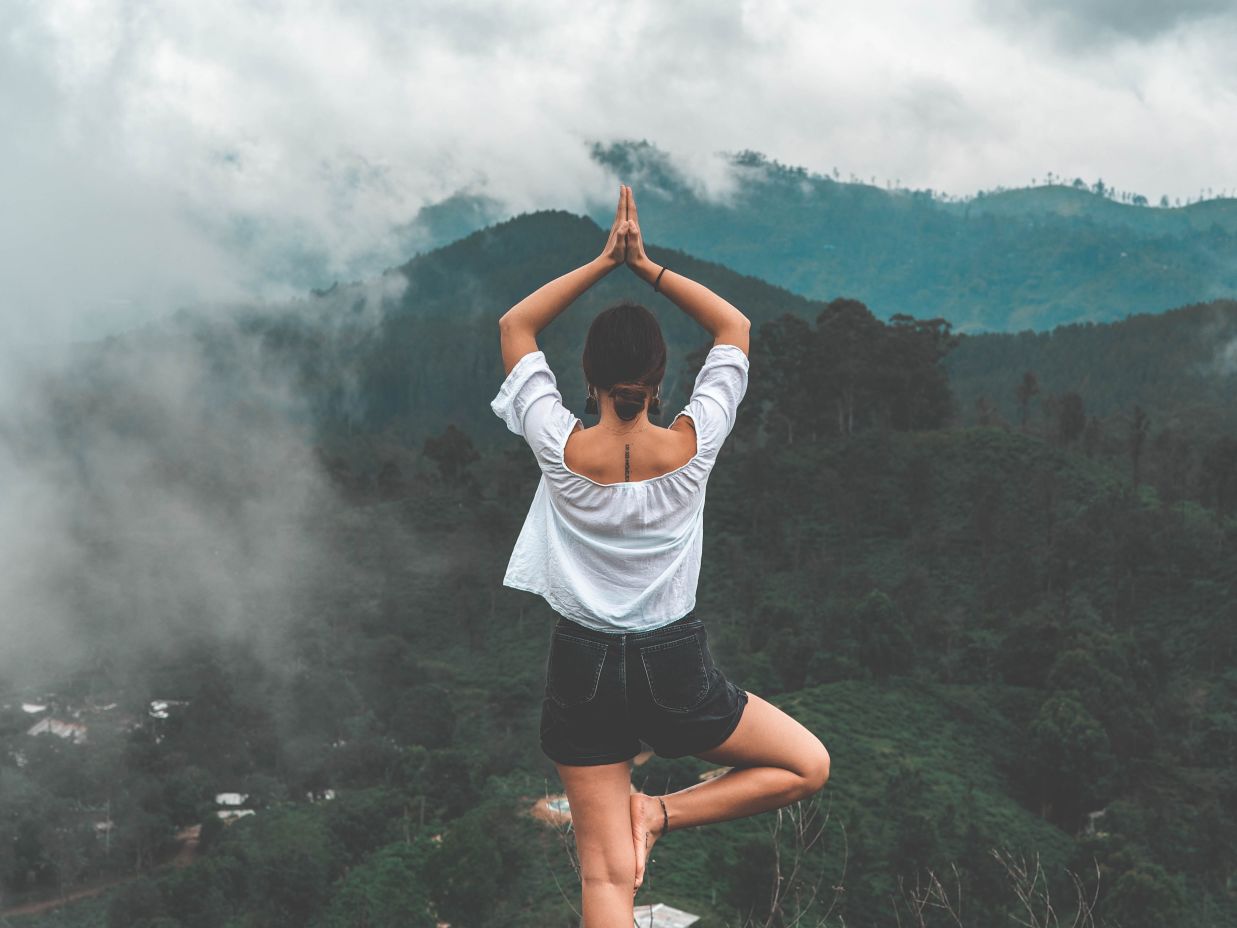 Image of a woman performing the Tree pose yoga move on a ledge that overlooks the cliff