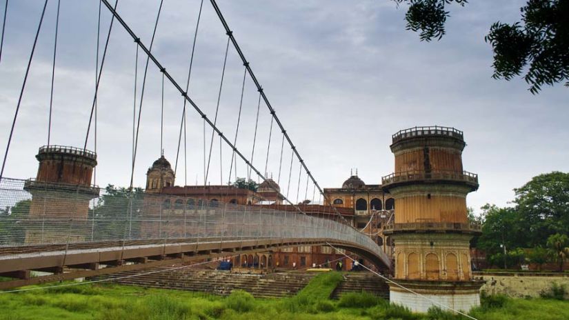 A hanging bridge leading to the Sheesh Mahal with greenery at the bottom