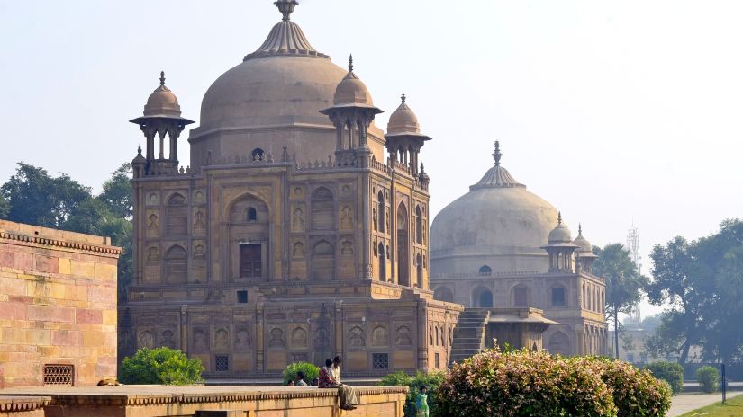 A domed sandstone mausoleum in a garden setting under a clear sky.