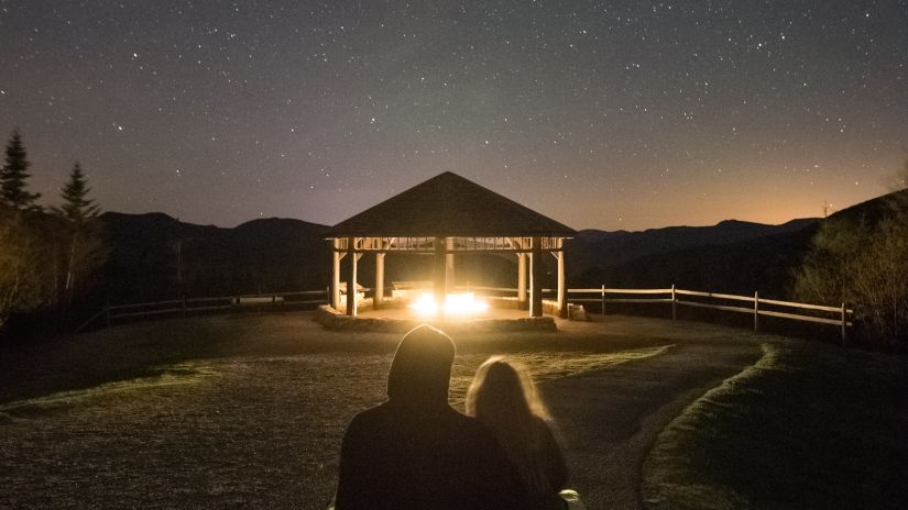 a couple sitting cuddled together on a carpet on the floor and stargazing the night sky