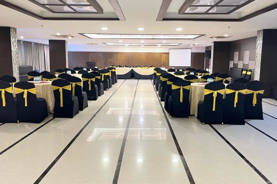 alt-text A wedding/banquet hall shot from behind with black chairs wrapped with golden bows