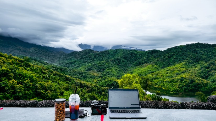 a laptop and other accessories set on a balcony overlooking lush mountains