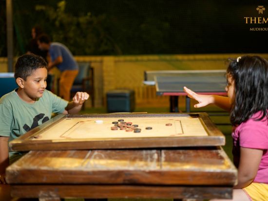 Two kids playing carrom at Themis Mudhouse - A Nature's Retreat Resort & Wellness