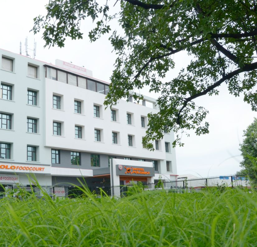 Hotel's facade  viewed from behind vibrant green foliage | Max Hotel Prayagraj.