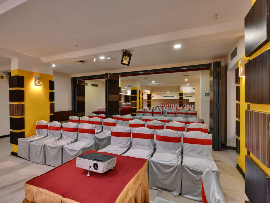 alt-text A banquet hall with grey and red covered chairs and a projector placed on a table - Click Hotel Yuvraj, Surat