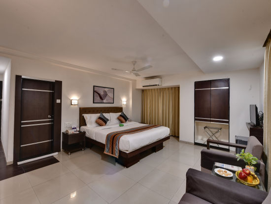 alt-text Another view of a superior room with a large bed, two lamps hanging above it, two comfortable chairs and an attached bathroom - Click Hotel Yuvraj, Surat