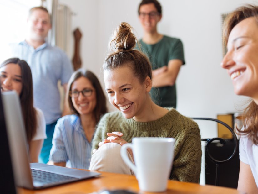 a group of people watching a laptop screen with smiles on their faces