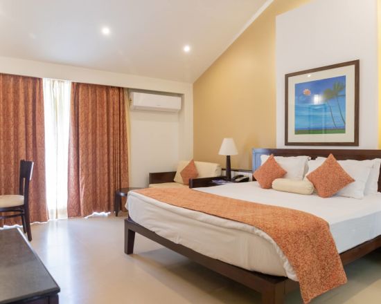 alt-text The king size bed in the premier room with peach coloured blanket at Kyriad Prestige Calangute, Goa