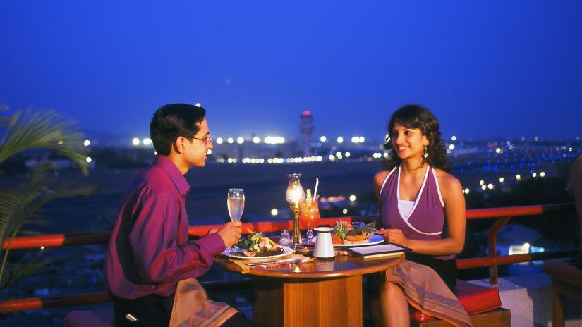 Orchid Hotel Mumbai Vile Parle - Image of a couple sitting at a table on an open roof restaurant and enjoying a meal at night time