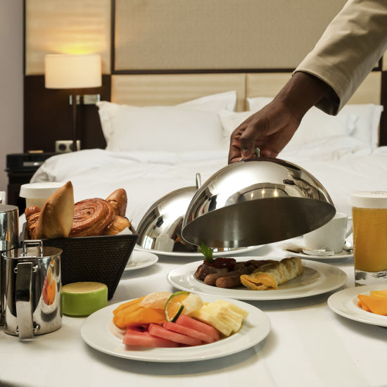 a person opening the cloche to relish breakfast that is served on bed